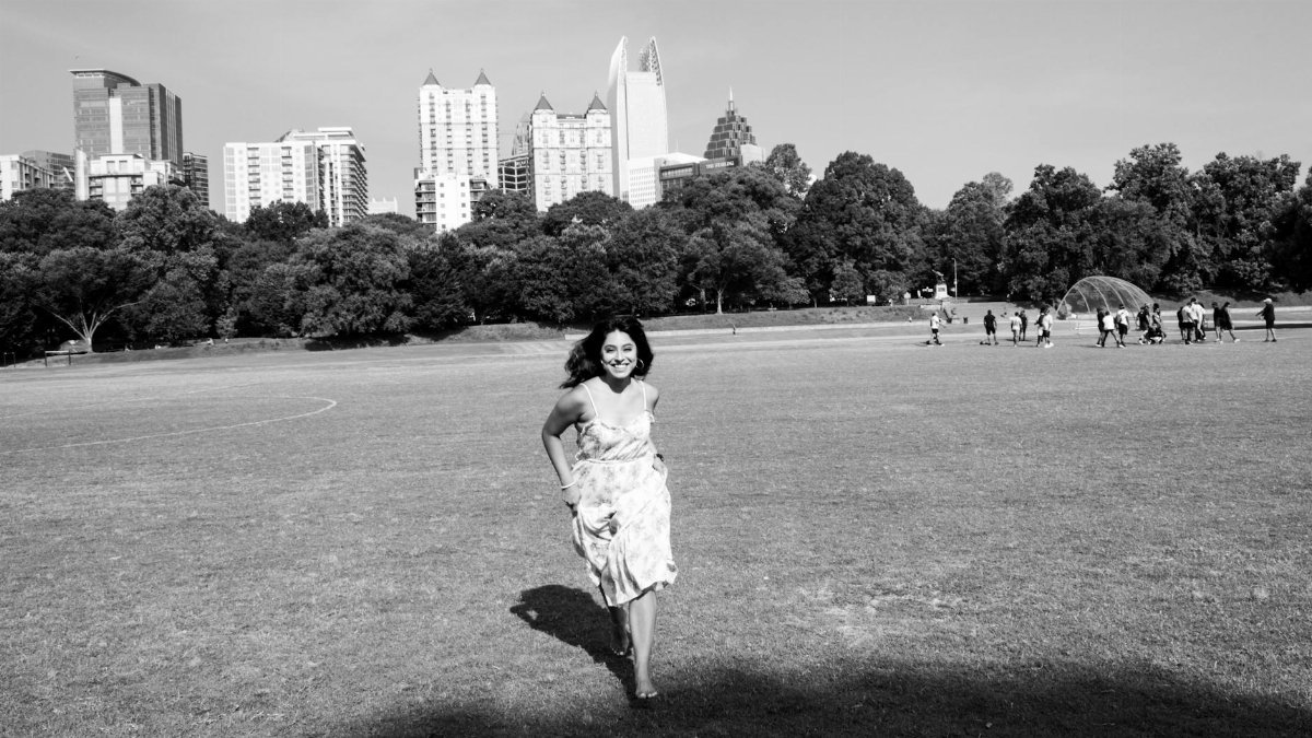 A joyful woman running in Piedmont Park with Atlanta skyline in background.