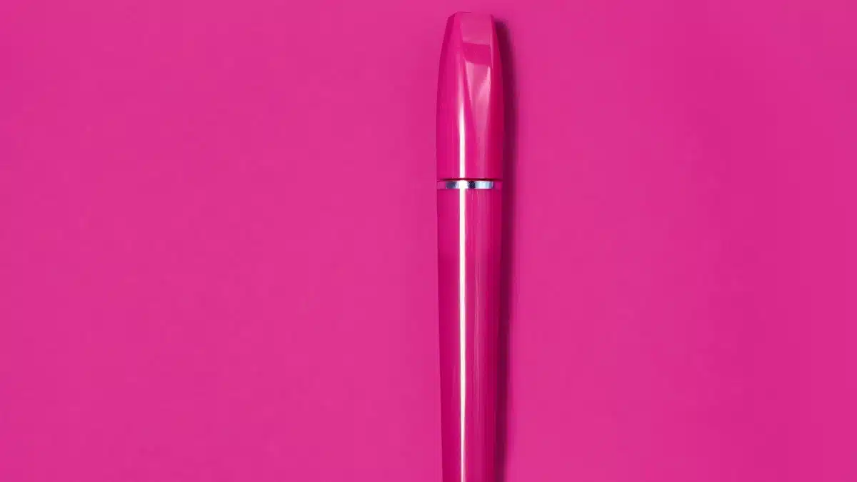 A striking pink mascara tube centered on a solid pink background, showcasing modern beauty packaging.