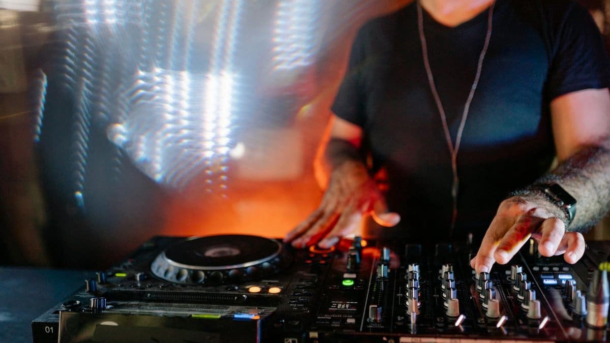 DJ playing music with turntables and colored lights in a lively nightlife setting.