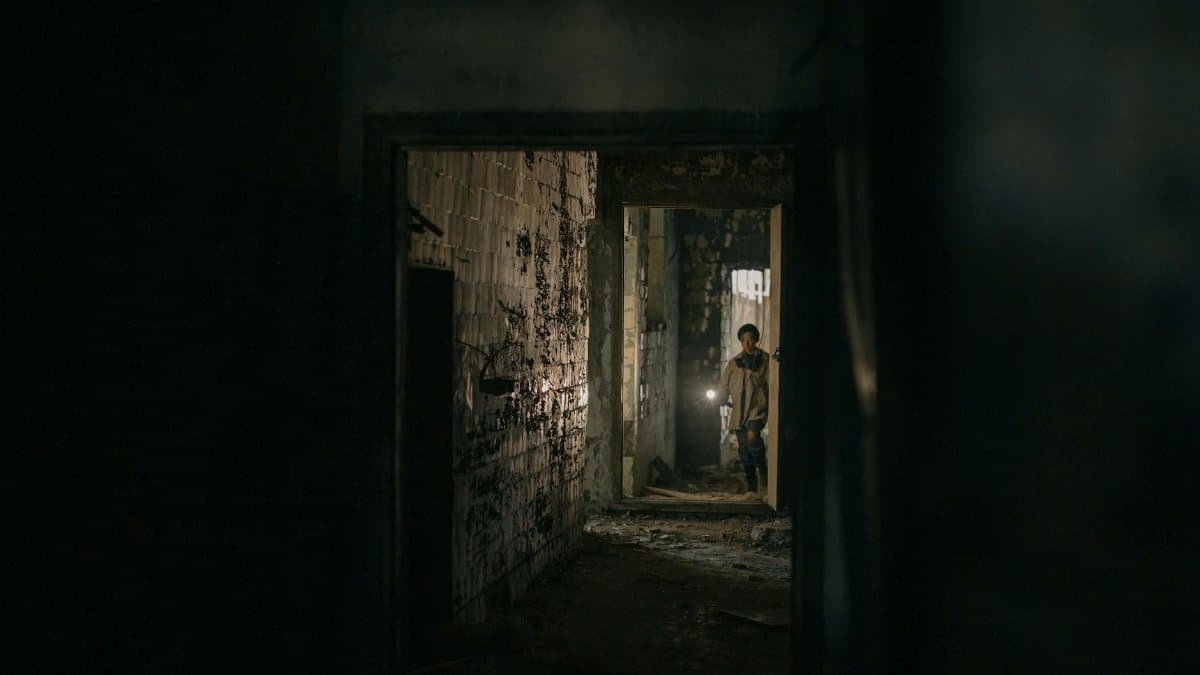 A young man with a flashlight explores a dark, abandoned urban corridor, representing desolation and survival.