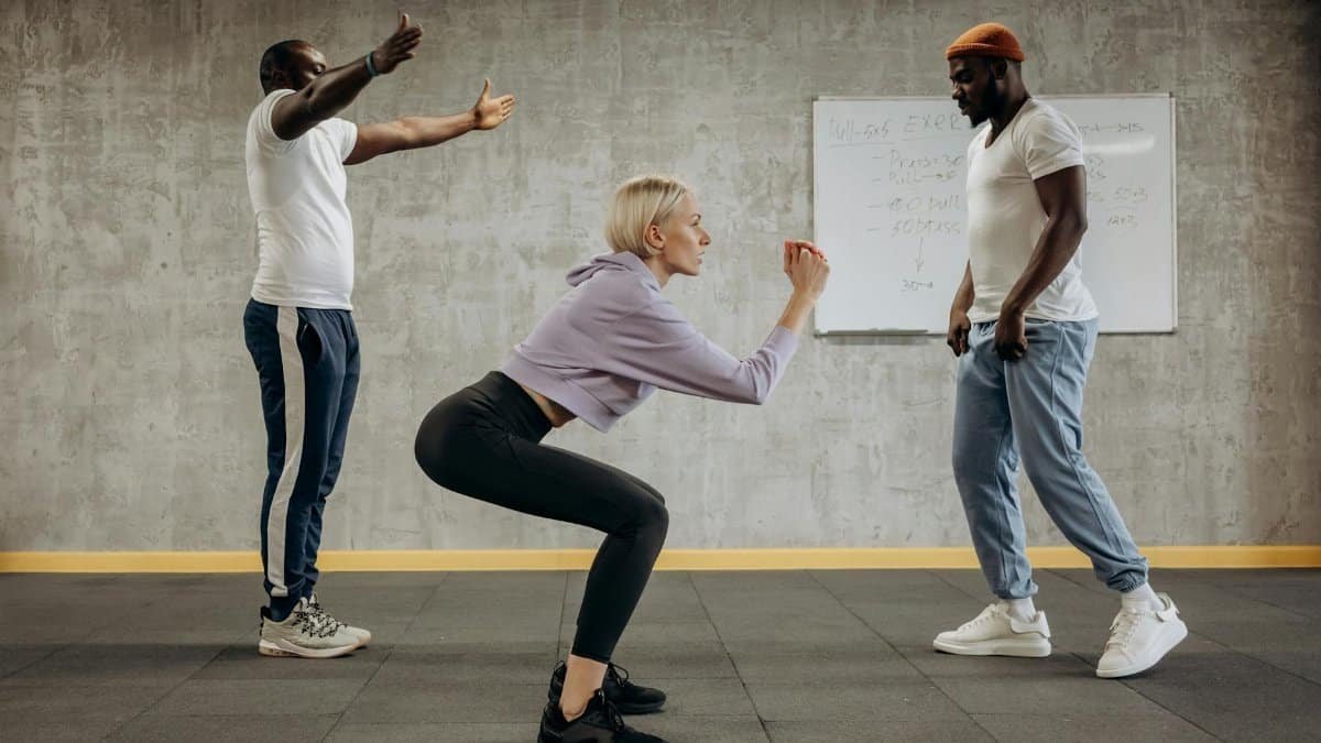 Three diverse adults engaged in a fitness class, focusing on squatting techniques indoors.
