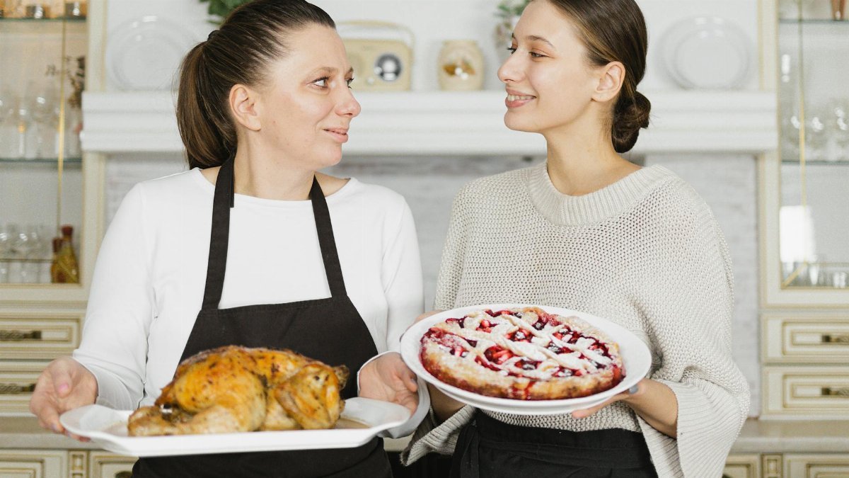 Mother and daughter bonding while baking together in the kitchen. Holding a pie and roasted chicken.