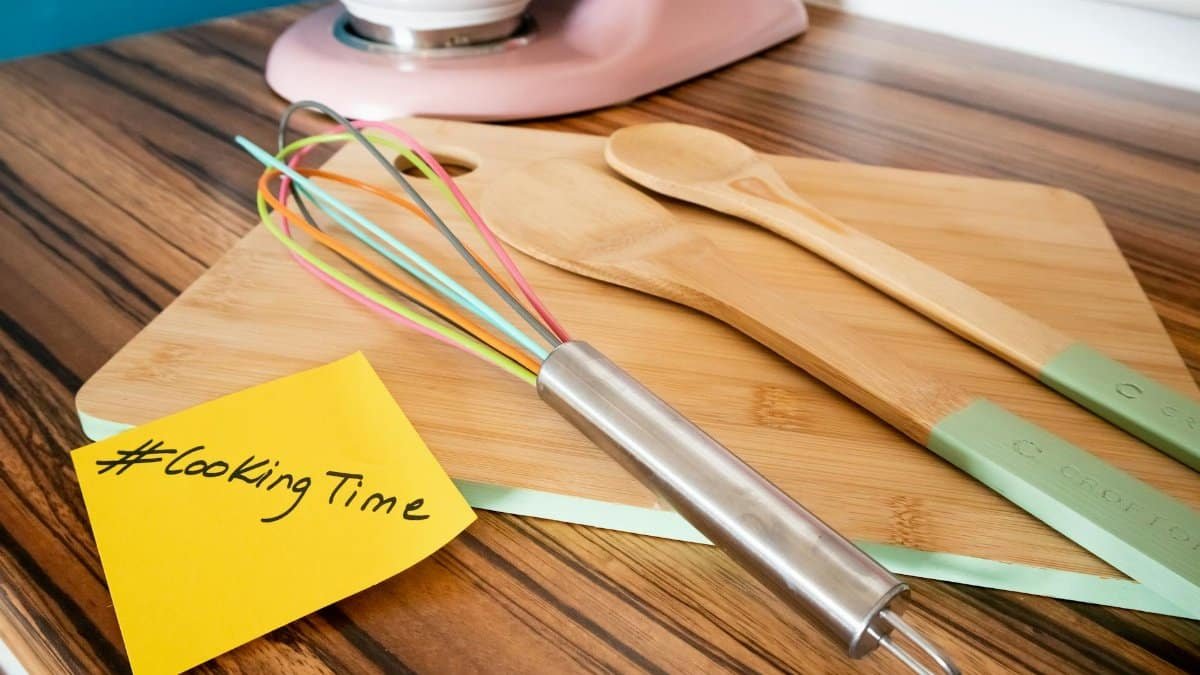 Colorful kitchen utensils on a bamboo cutting board with a cooking hashtag note, perfect for culinary themes.