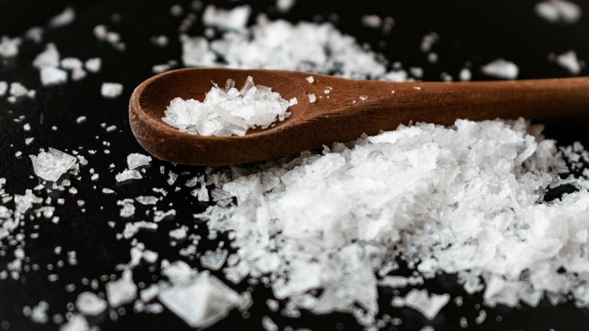 Closeup of wooden spoon arranged with sea salt scattered on table in kitchen