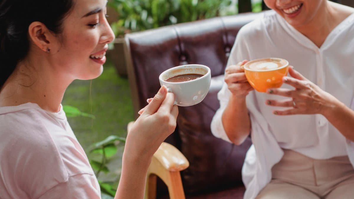 Two women enjoying hot beverages in a cozy indoor setting, sharing smiles and relaxation.