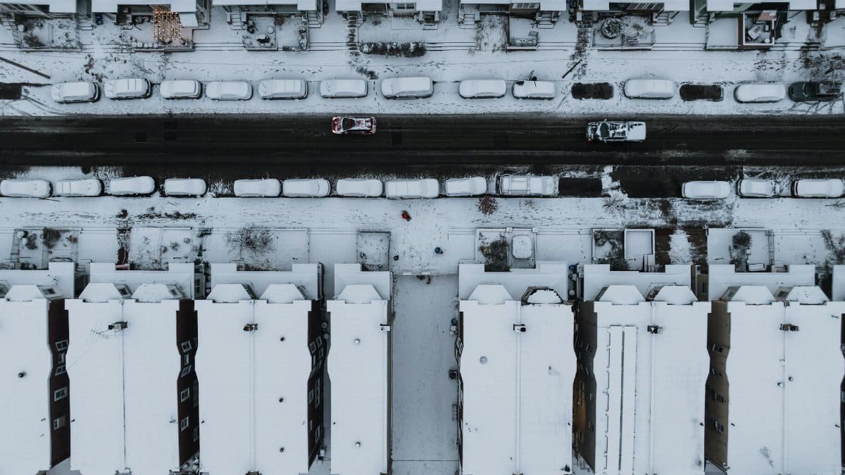 Aerial view of snow-covered street in Philadelphia, showcasing rooftops and parked cars.