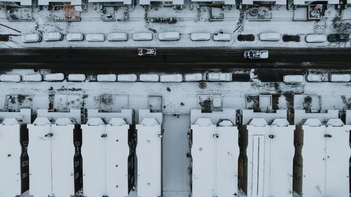 Aerial view of snow-covered street in Philadelphia, showcasing rooftops and parked cars.