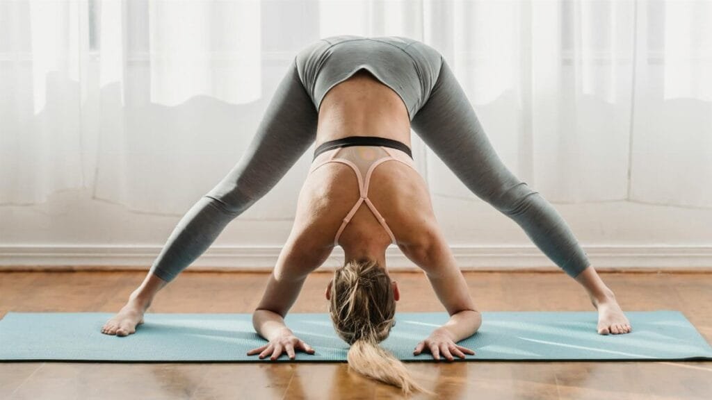 Fit female in sportswear doing yoga in Prasarita Padottanasana pose with bent back on mat in light room