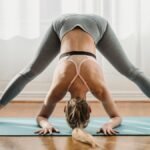 Fit female in sportswear doing yoga in Prasarita Padottanasana pose with bent back on mat in light room