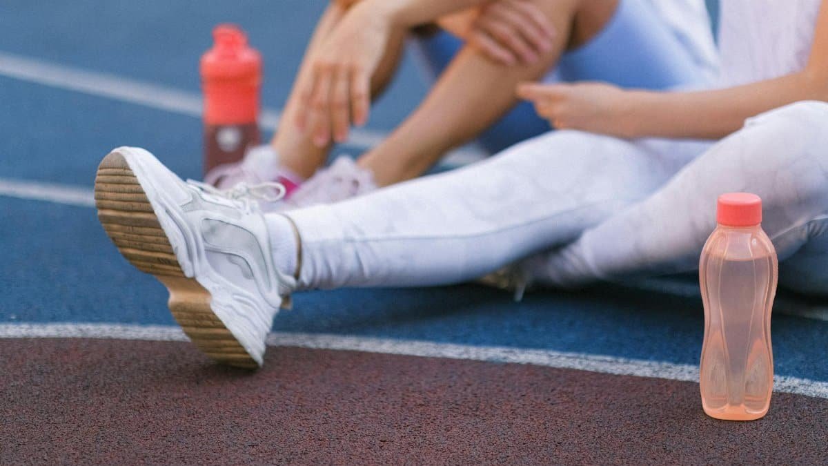 Two women relaxing with water bottles on a sports track, wearing activewear.