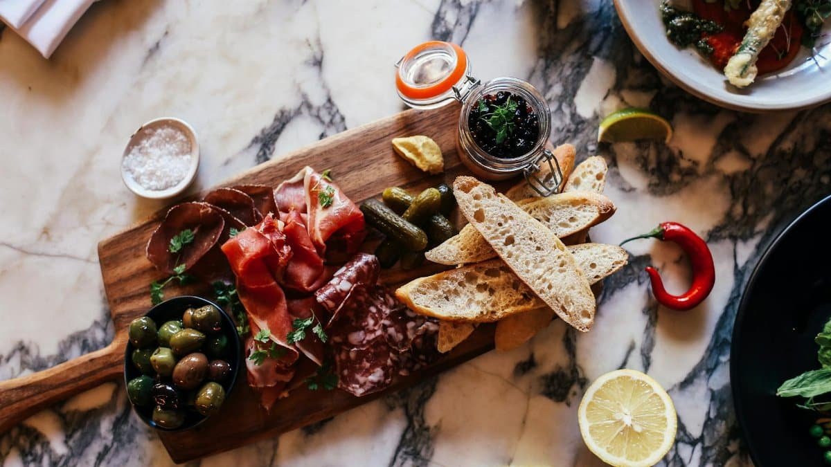A rustic charcuterie board with meats, olives, and bread on a marble table.