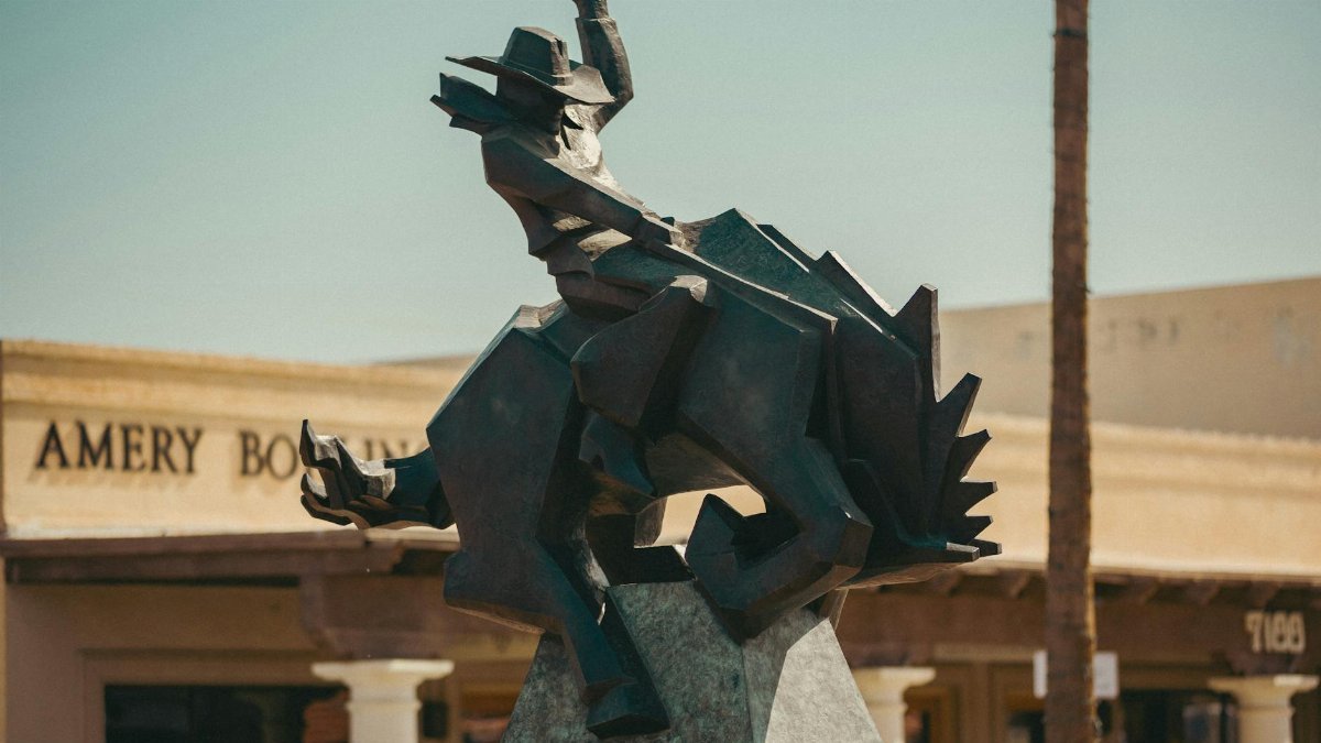 Dynamic bronze sculpture of a cowboy on a horse outdoors, under bright daylight.