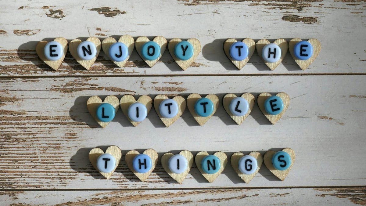 Heart-shaped letters spelling 'Enjoy the Little Things' on a rustic wooden background for inspirational decor.