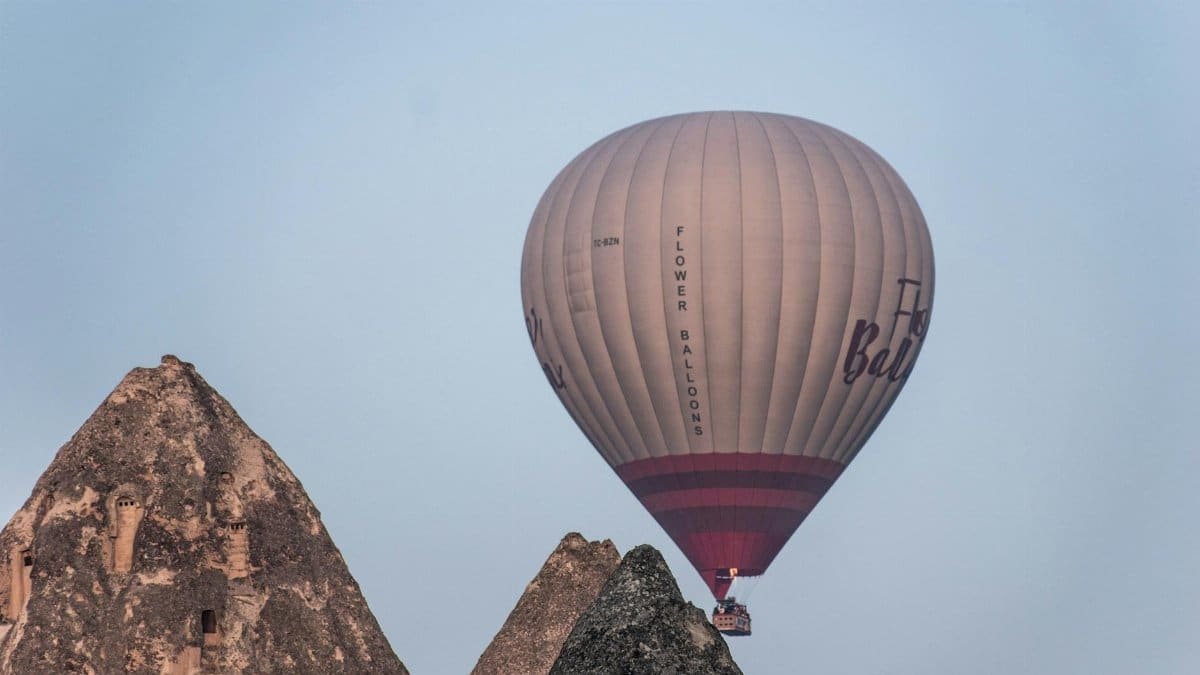 Hot air balloon soaring over Cappadocia's unique rock formations during the day.