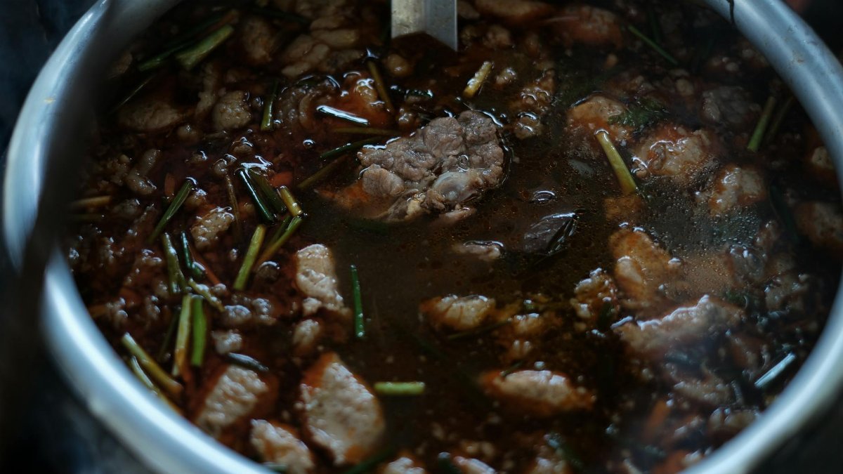 Close-up of a simmering beef stew with herbs and spices in a metal pot.