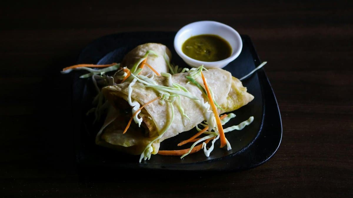 Tasty Indian wraps served with green chutney on a black plate, perfect for food lovers.