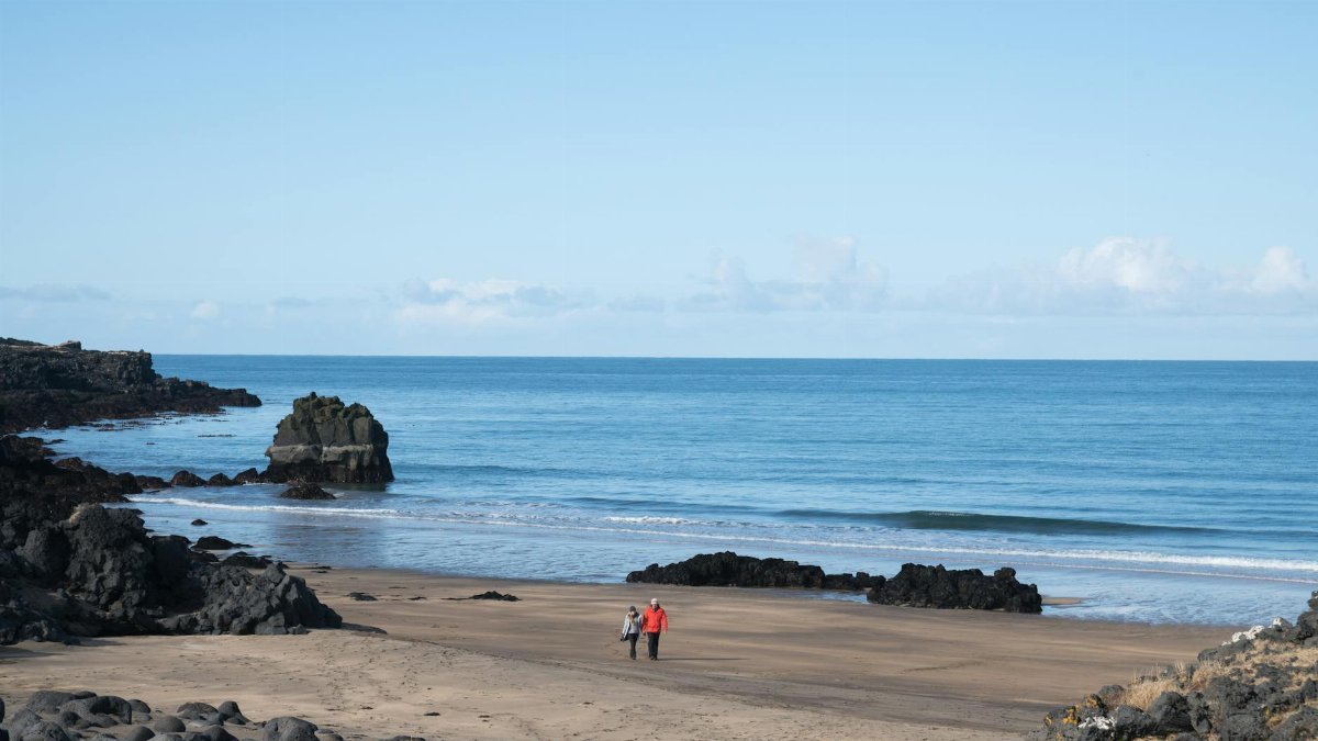 A serene seascape featuring a couple walking along a rocky beach under a clear blue sky.