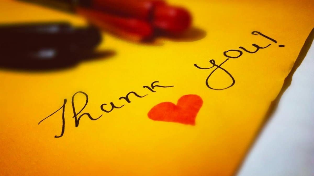 Close-up of a thank you note with a heart and pen on colored paper.