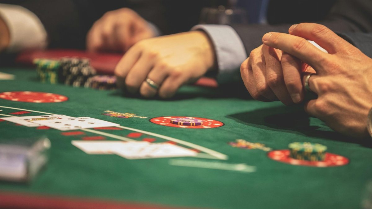Hands playing blackjack in a casino setting with cards and chips on a green table.