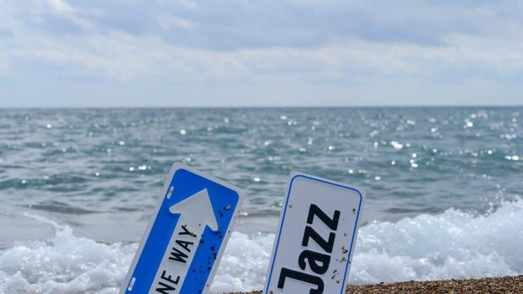 Jazz and One Way signs on a sandy beach with ocean waves.