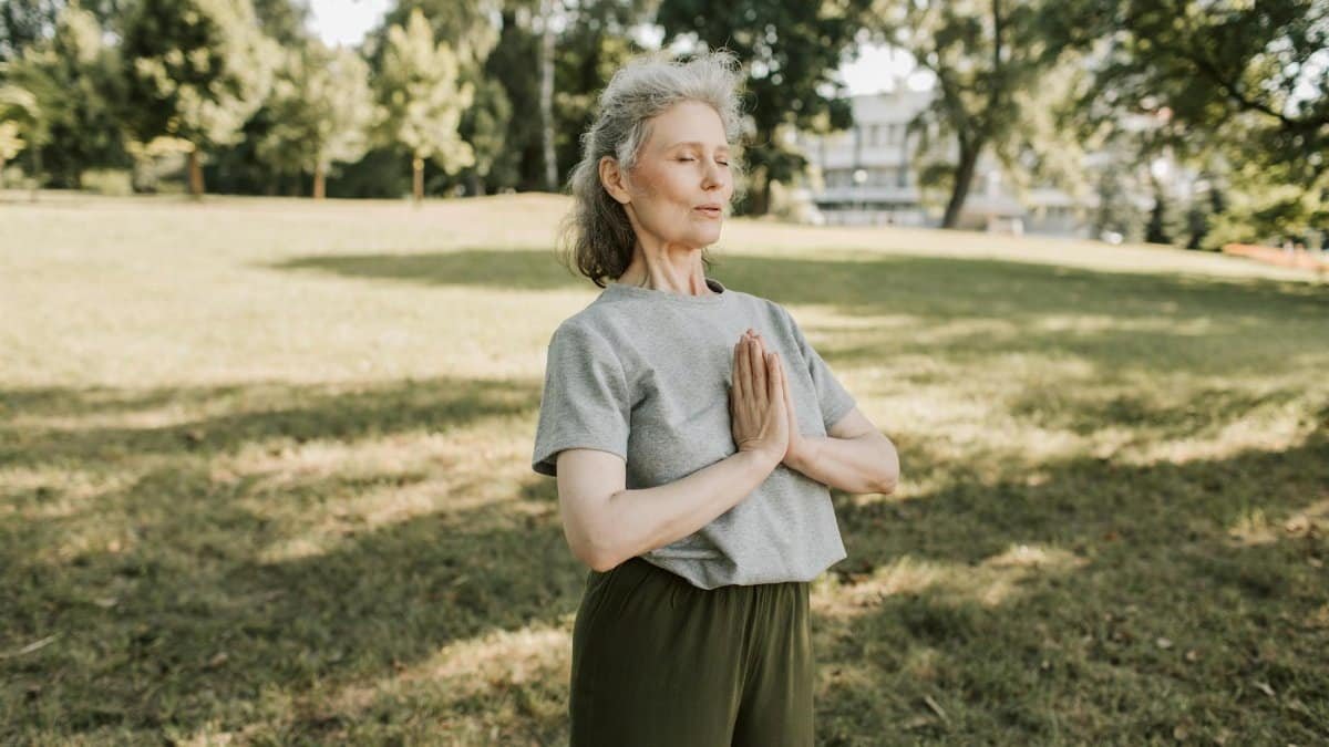 Elderly woman meditating and practicing yoga in a sunny park, embracing wellness and mindfulness.