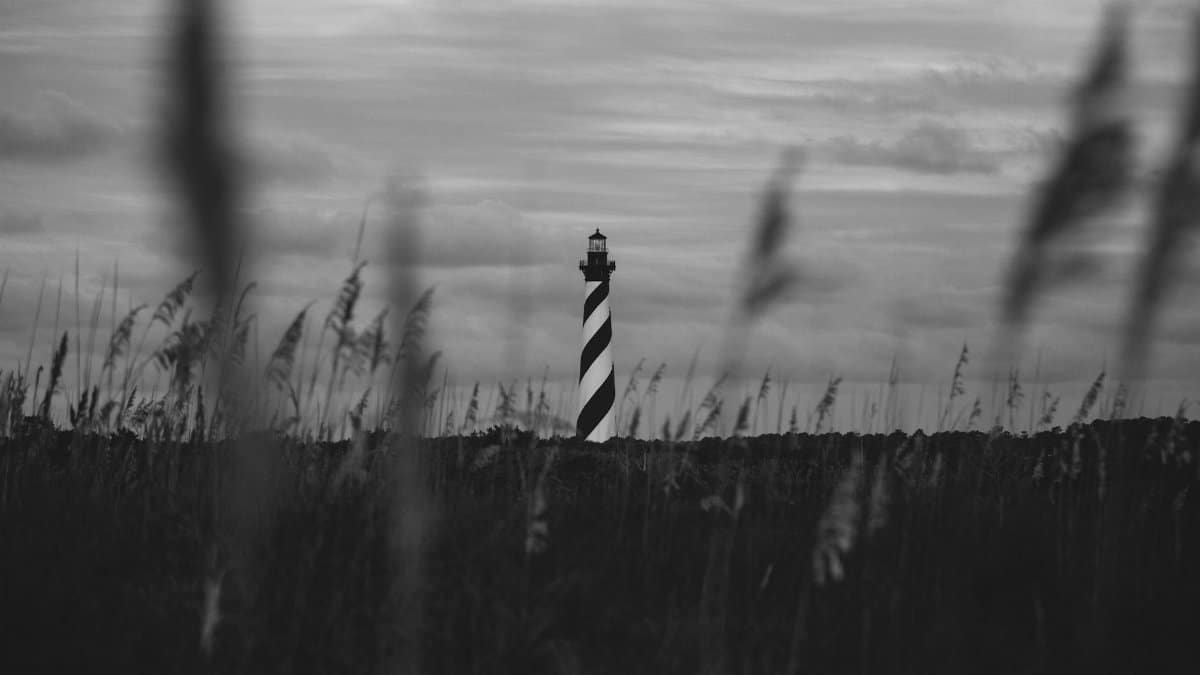 Scenic black and white photograph of Cape Hatteras Lighthouse in a rural field.