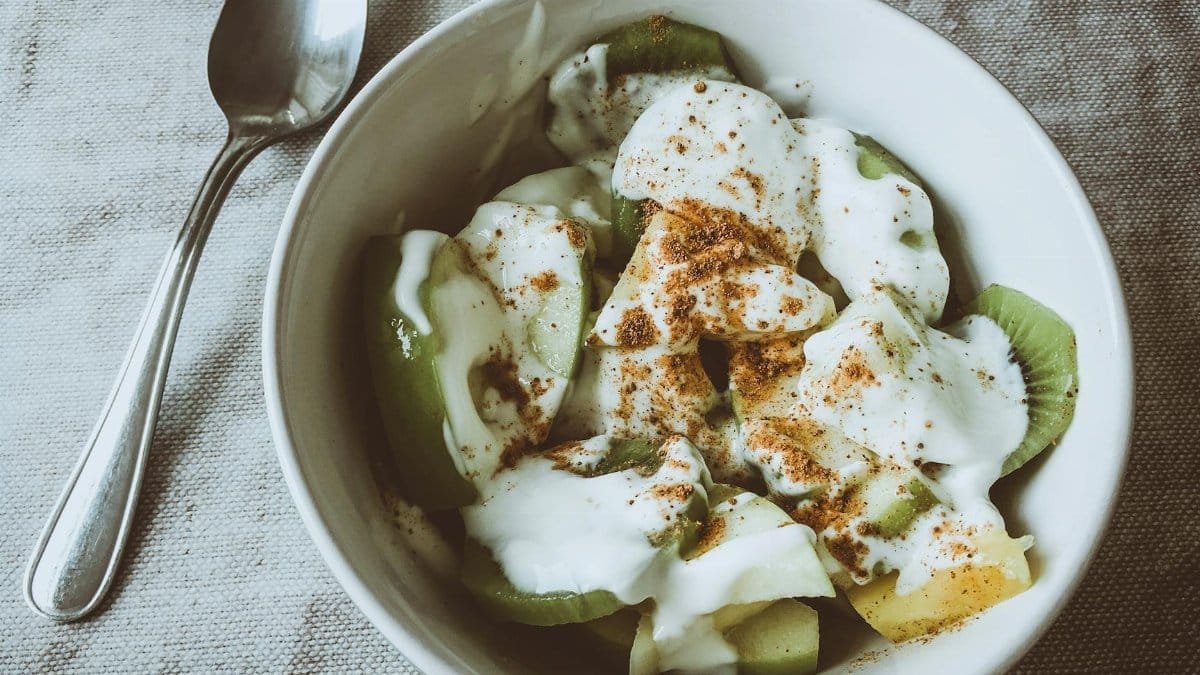 Fresh kiwi and pineapple slices topped with yogurt and cinnamon in a white bowl, perfect for a healthy breakfast.
