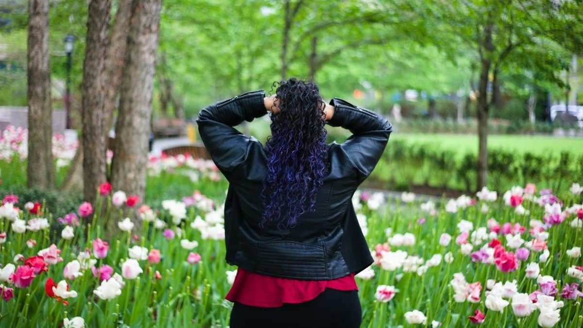 A woman with curly hair in a black jacket stands in a colorful flower field, enjoying spring in New York City.