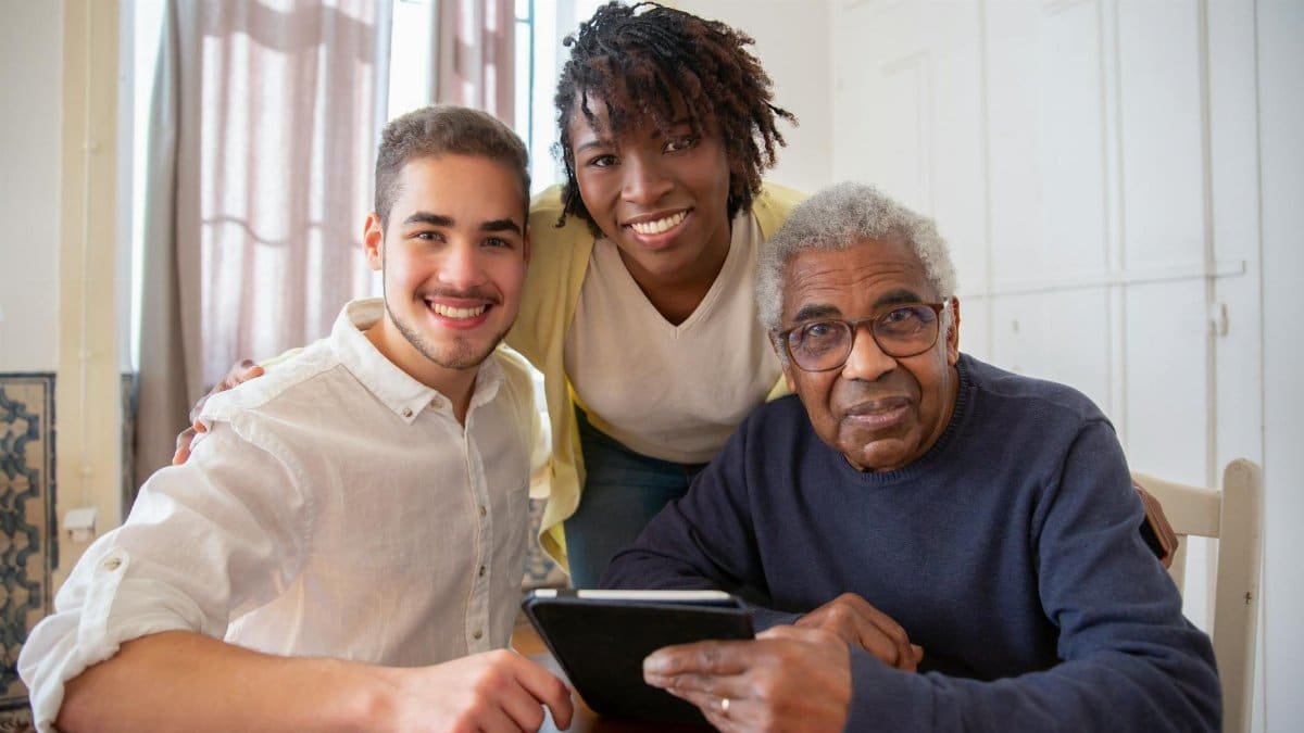 Elderly man enjoying technology with diverse caregivers at home.