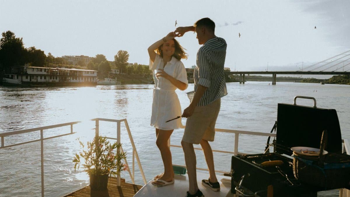 A couple enjoys a romantic dance on a yacht during a vibrant sunset with scenic river views.