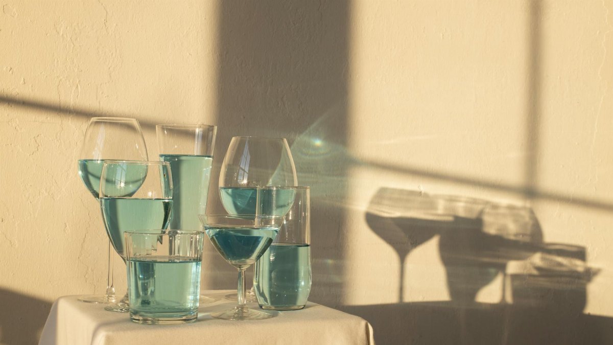 A collection of various glassware filled with blue liquid casting artistic shadows on a table.