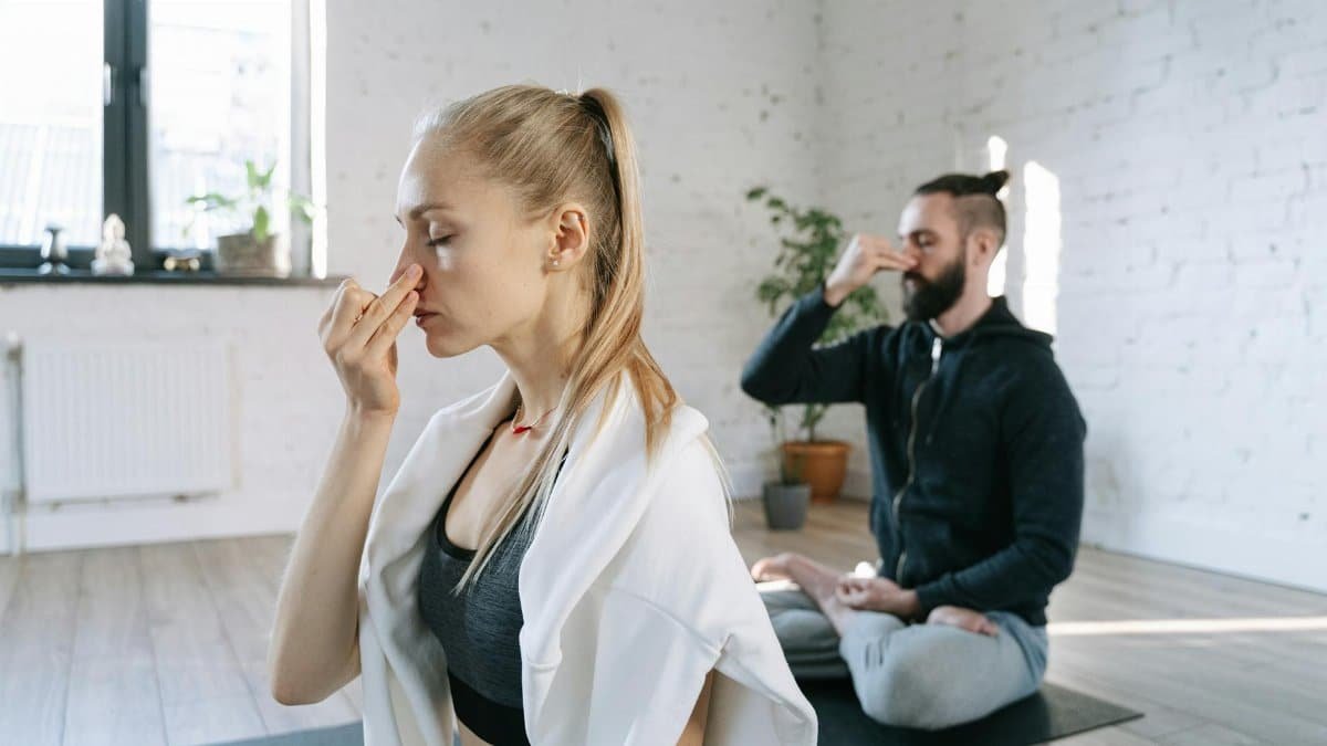 Two individuals practicing mindful breathing yoga in a serene indoor home setting.