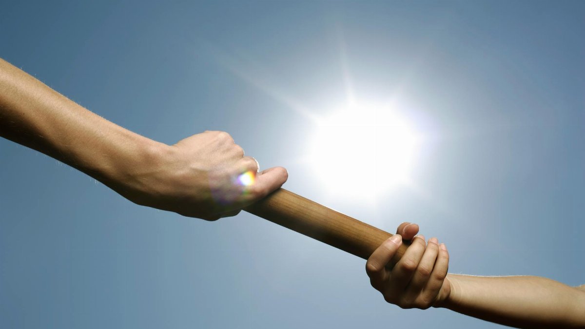 Close-up of hands passing a relay baton against a bright sunny sky.