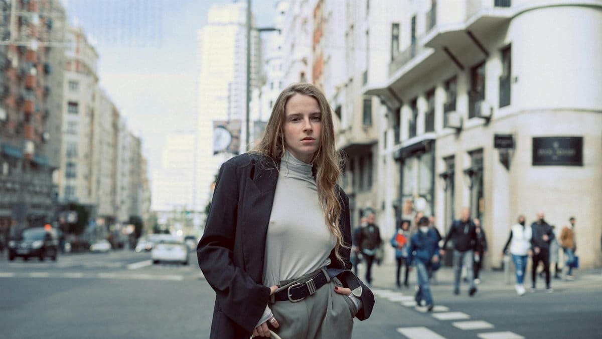 A young woman confidently poses in a bustling Madrid street, showcasing modern urban fashion.