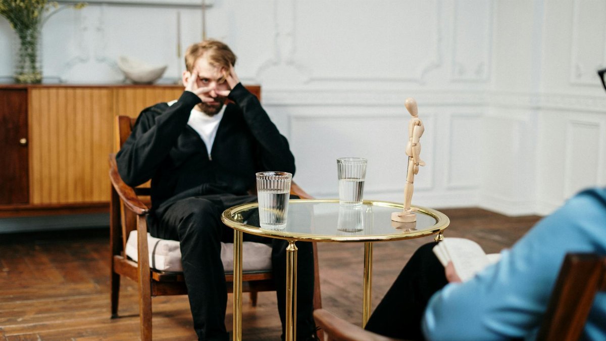Man consulting with therapist in a cozy, well-lit office. Emotional support and mental health focus.