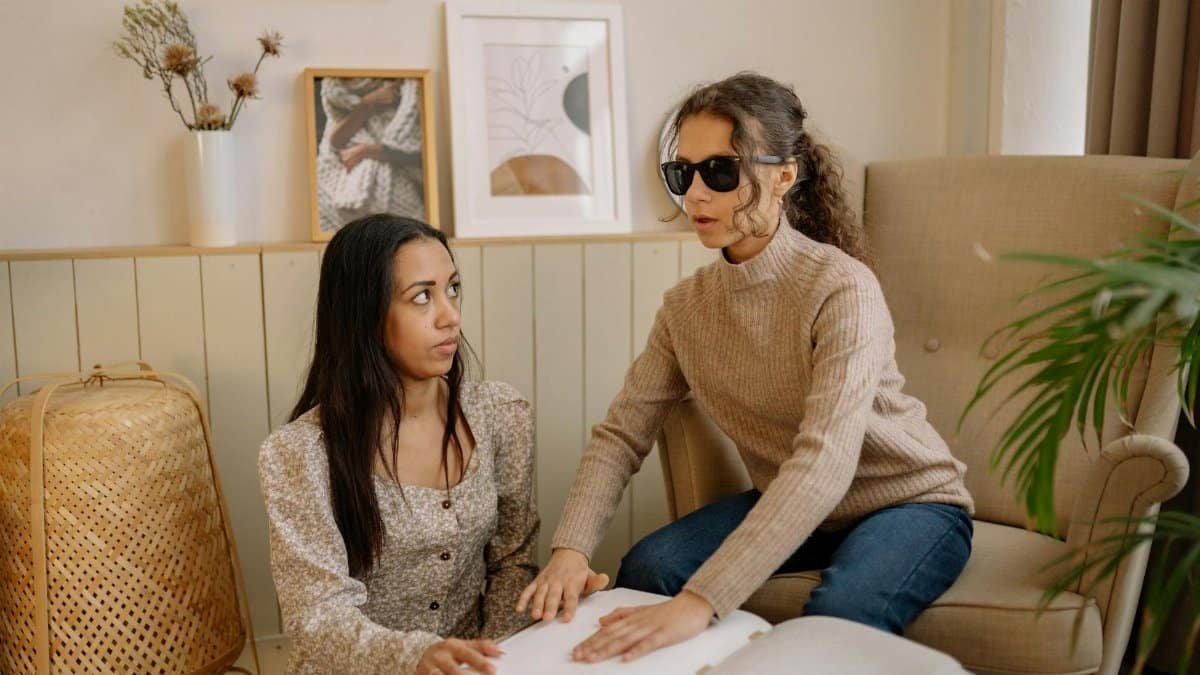 Two women reading a Braille book inside a cozy room, fostering educational connection.