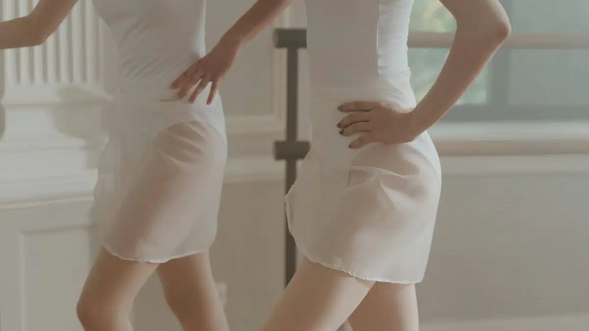 Elegant ballet dancers in white leotards and skirts practicing indoors.