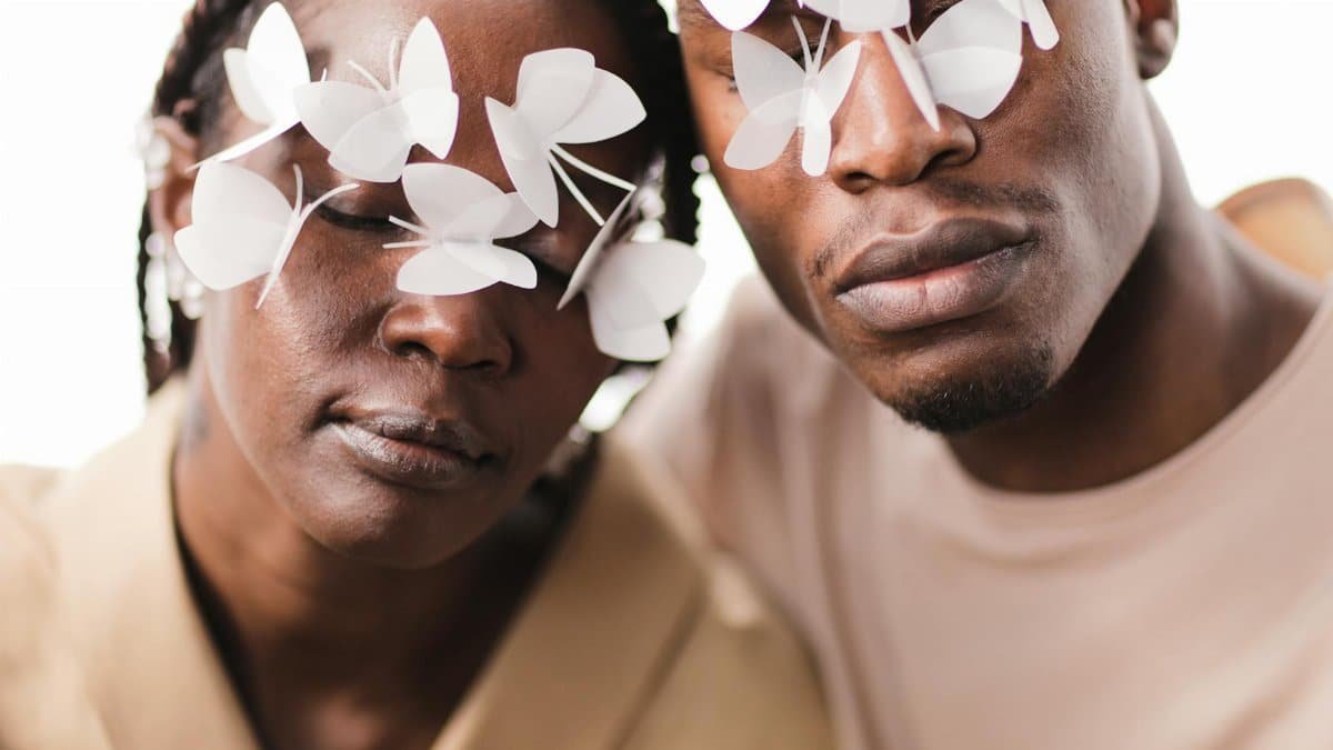 Artistic portrait of a man and woman with paper butterflies over eyes, symbolizing vision.