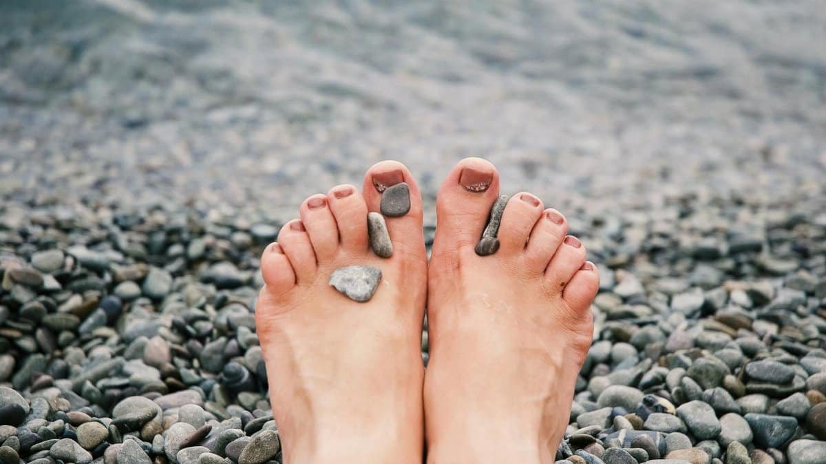 Close-up of female feet with stones on pebbled beach by the water, evoking relaxation and tranquility.