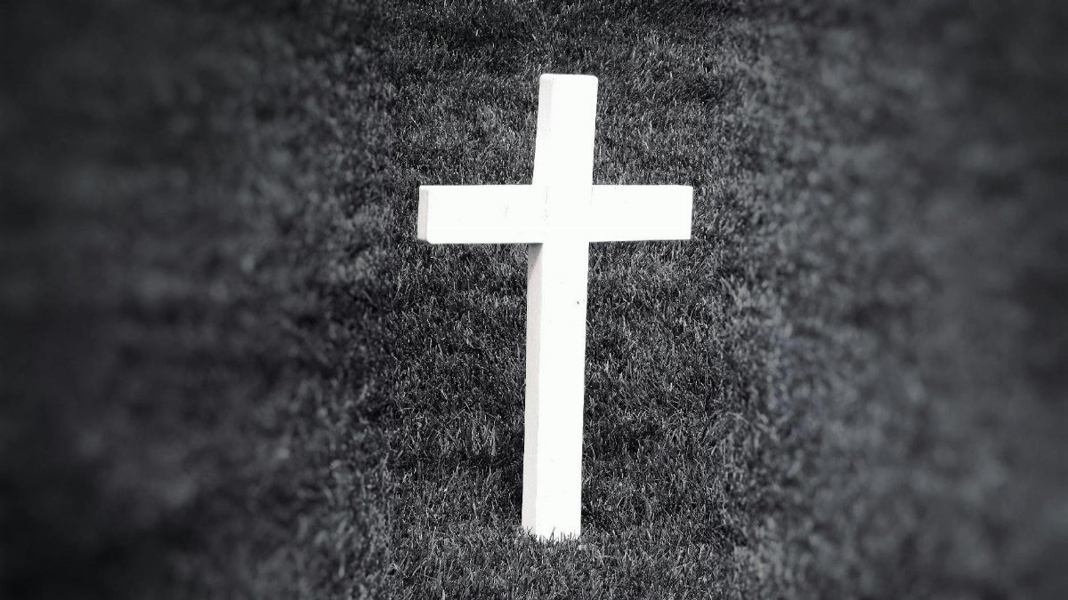 Black and white image of a cross standing in grass, symbolizing spirituality and remembrance.