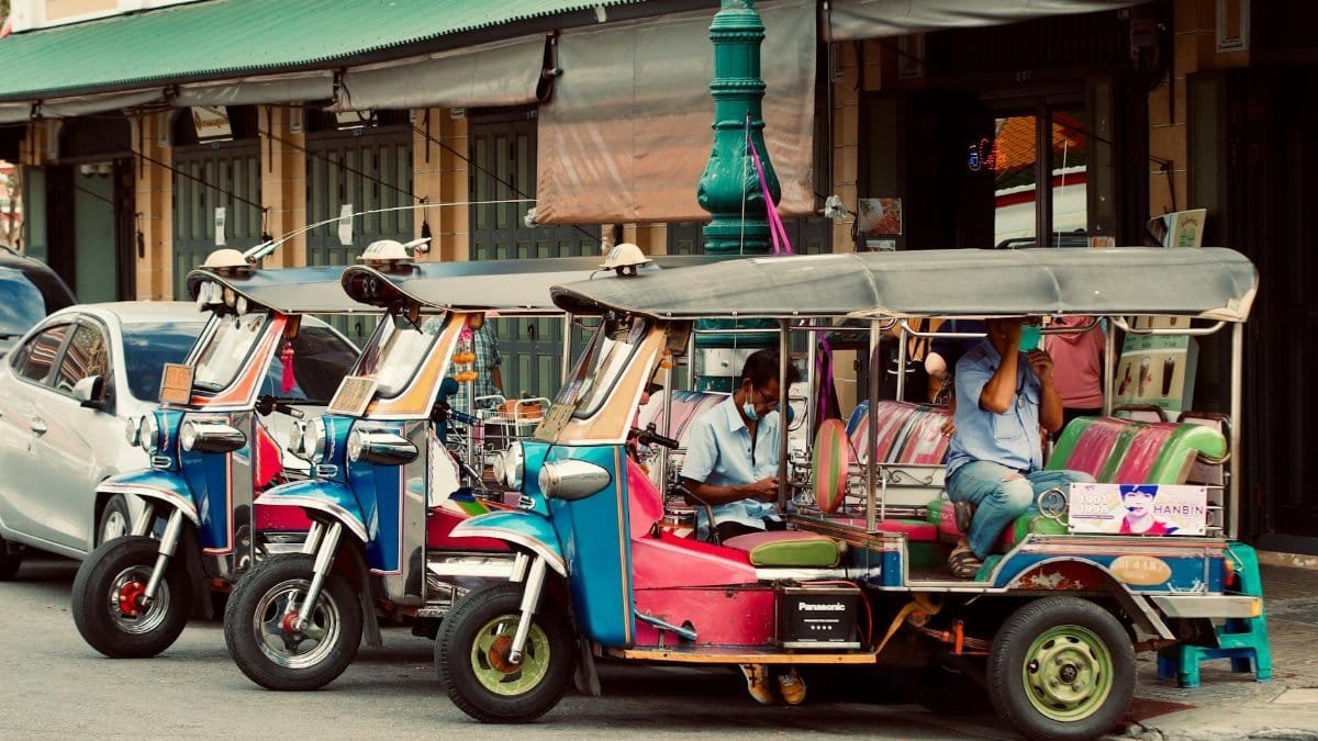 A vibrant scene of Tuk-Tuks parked on a bustling city street with drivers.