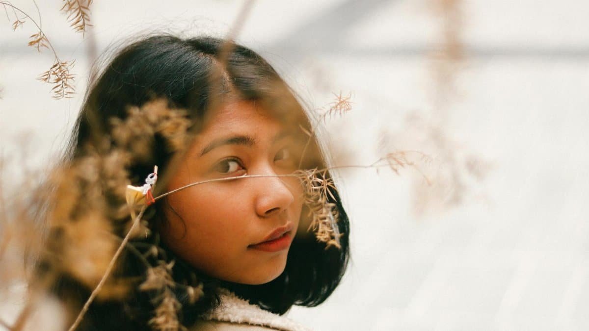 A thoughtful portrait of a woman with natural elements blending into the frame, creating an artistic effect.