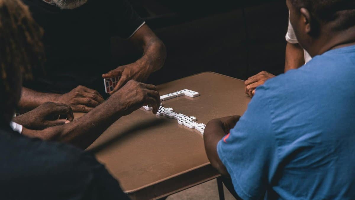 A group of senior men playing dominoes on a table indoors, engaging in recreation and strategy.