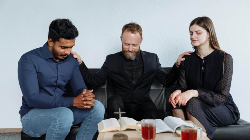 Diverse group of adults sitting together, praying and reading the Bible indoors.
