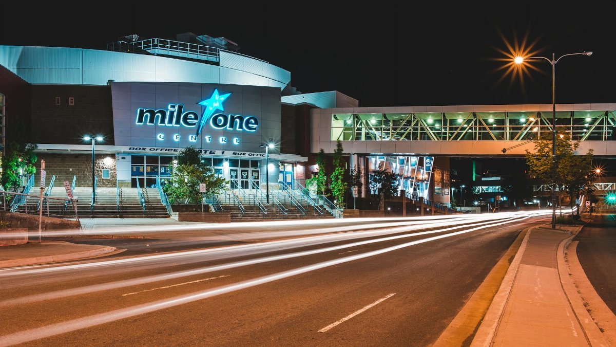 Illuminated Mile One Centre with dynamic vehicle light trails at night, showcasing urban architecture.
