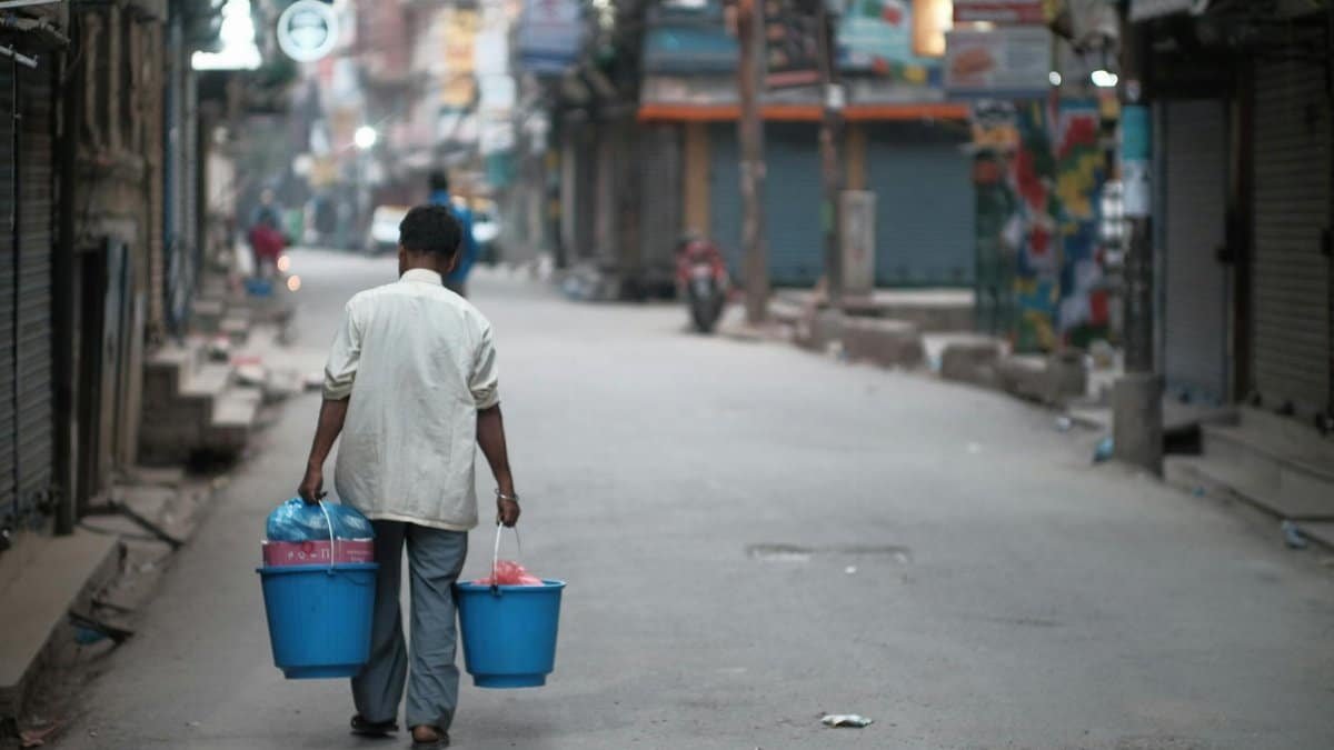 A man walks down a deserted city street carrying two plastic buckets.