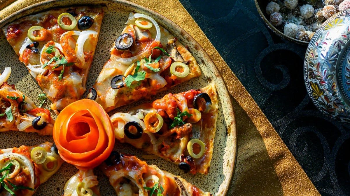 Top view of a vibrant Italian pizza with olives, onions, and a rose garnish, set on a golden tablecloth.