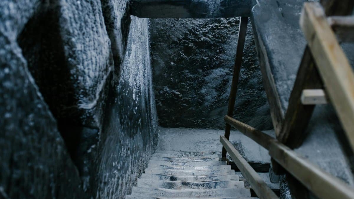 From above of aged stone stairway covered with salt in ancient cave with shabby walls and wooden railings in Registry Chamber of Salina Turda mine