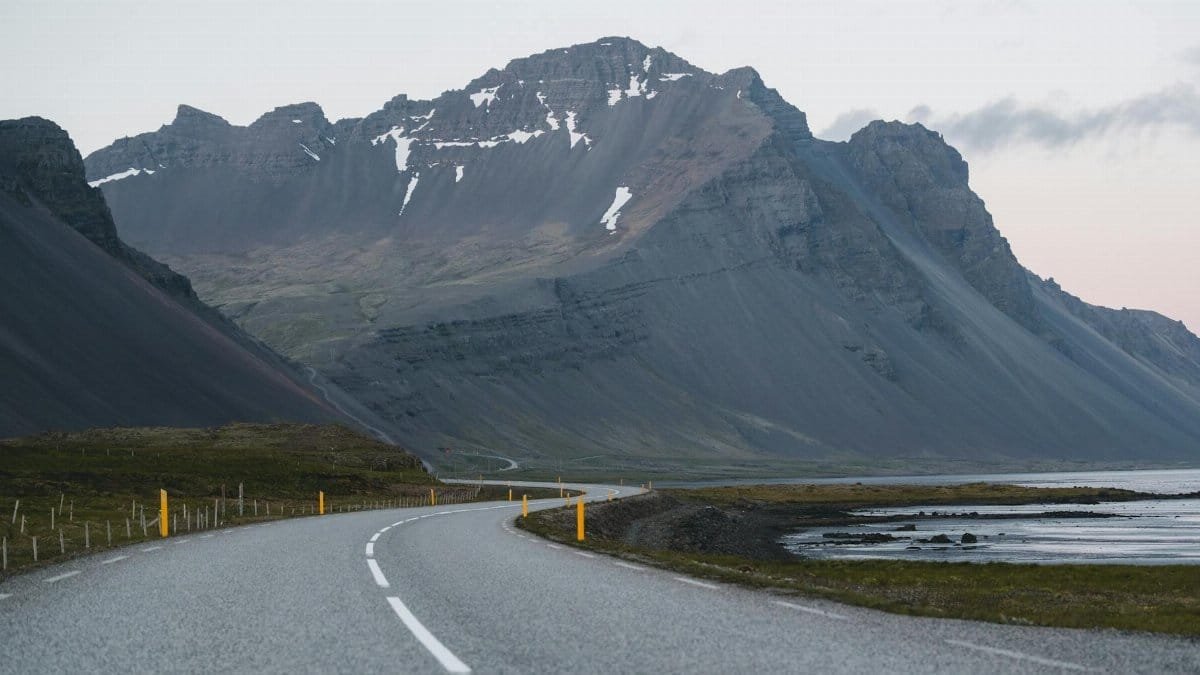 A winding road leading through Icelandic mountains, offering a serene and picturesque landscape at dusk.