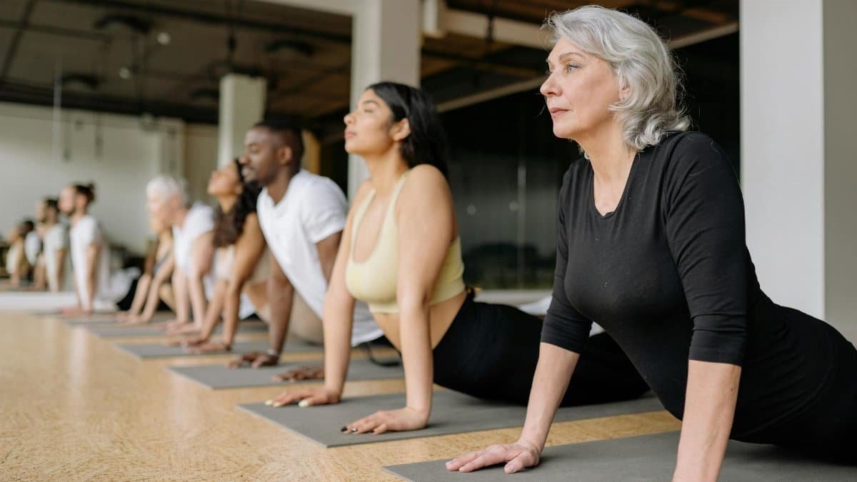 A diverse group of adults in a yoga class, practicing stretching on mats indoors.